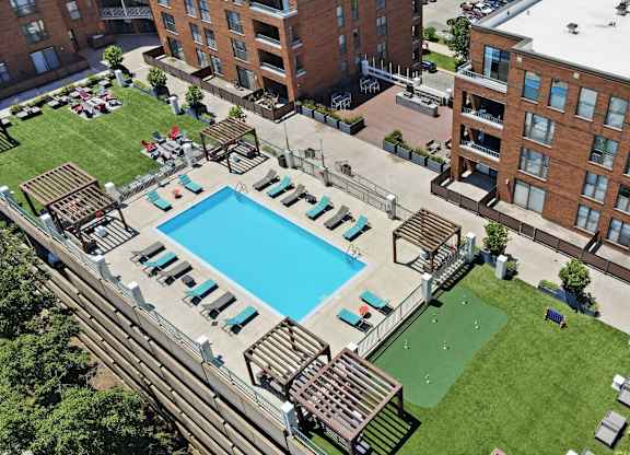 An aerial view of a building with a rooftop pool in the middle and social deck with AstroTurf, firepits, grills, and assorted seating around it.