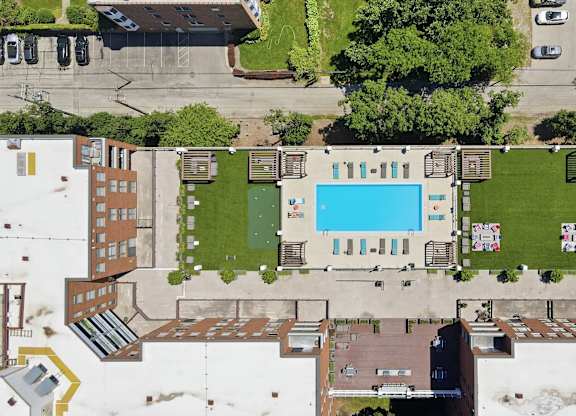 An aerial view of a building with a rooftop pool in the middle and social deck with AstroTurf, firepits, grills, and assorted seating around it.