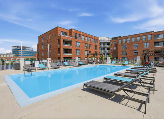 A large rooftop swimming pool with sun loungers in front of a red brick building.
