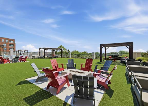 A set of red and blue adirondack chairs surrounding a fire pit with assorted rooftop seating in the background.