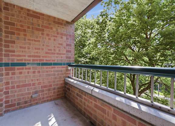 A balcony with a brick wall and green metal railing.