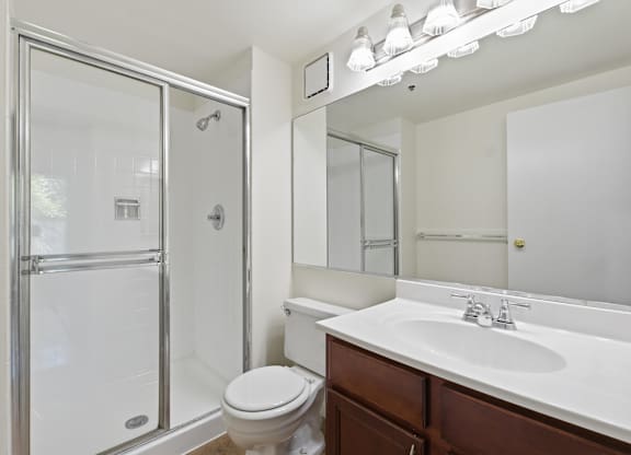 A white bathroom with a toilet, sink, mirror, and standing glass shower.