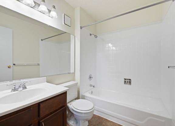 A white bathroom with a toilet, sink, mirror, and tiled bathtub.