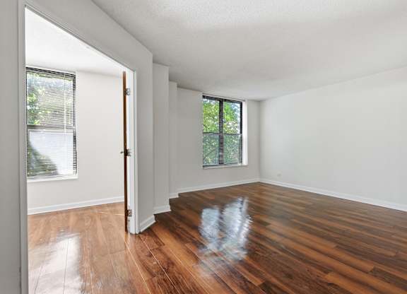 A bedroom with wooden floors, window, and attached den.