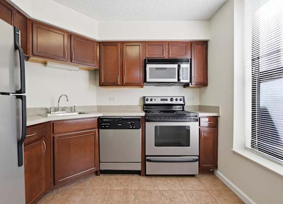 A kitchen with brown cabinets and a stainless steel appliances: microwave, stove, dishwasher, and fridge.