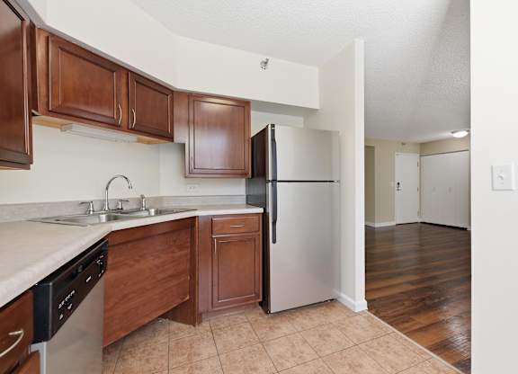A kitchen with brown cabinets and a stainless steel appliances: dishwasher and fridge.