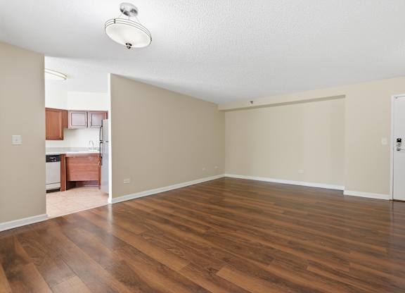A living room with kitchen in the background that has brown cabinets and stainless steel appliances.