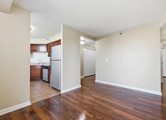A living room with kitchen in the background that has brown cabinets and stainless steel appliances.