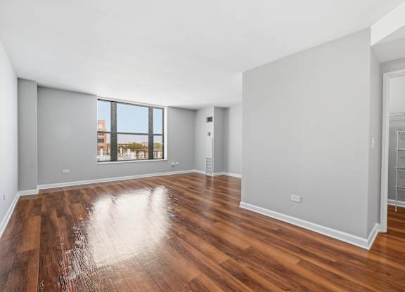 A renovated studio living and bedroom space with wooden floors and window.
