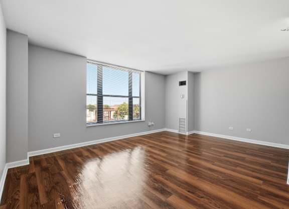 A renovated studio living and bedroom space with wooden floors and window.