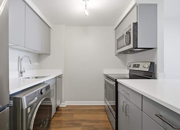 A renovated kitchen with a stainless steel refrigerator, microwave, oven, and 2-in-1 washer/dryer.