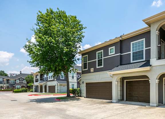A tree stands in front of a grey and white two story apartment building.