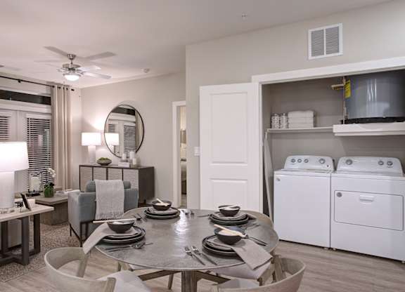A modern dining room with a table set for four and a washer and dryer in the background.