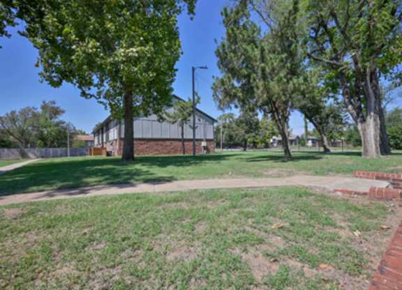 A park with a building in the background and a brick wall on the right.
