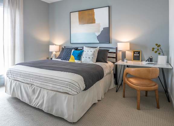 A bedroom with a bed, desk, chair, and a ceiling fan.