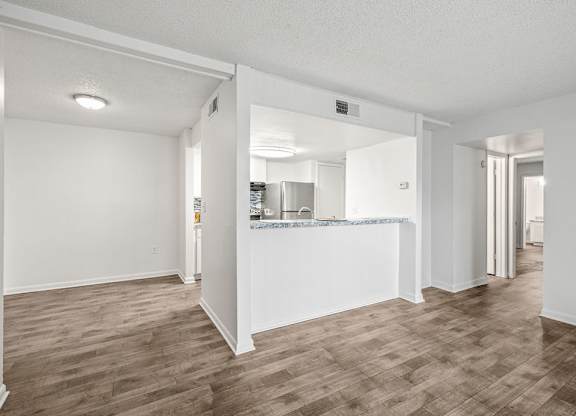 an empty living room with a kitchen in the background