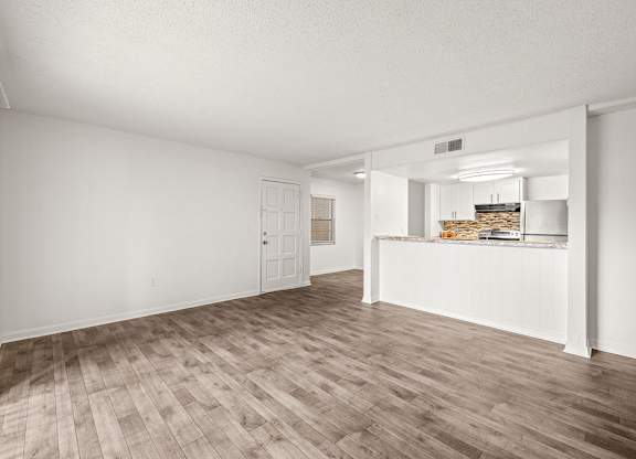 an empty living room and kitchen with wood flooring
