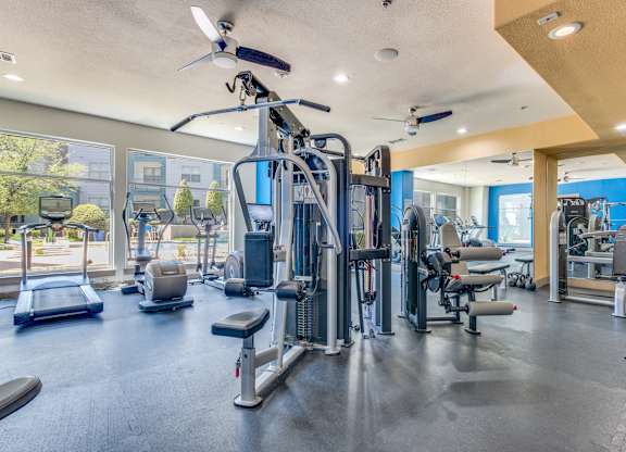 A spacious gym with a variety of equipment including treadmills, weight machines, and a ceiling fan.