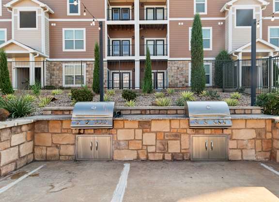 A wall of apartment buildings with a stone wall and grills in front.