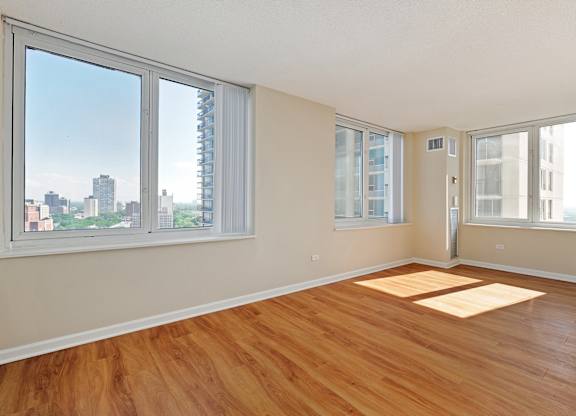 A room with wooden floors and a view of the city through the windows.
