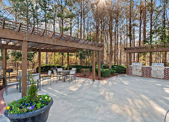 A patio with a wooden pergola and a planter with purple flowers.