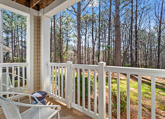 A white chair is on a porch with a view of a wooded area.