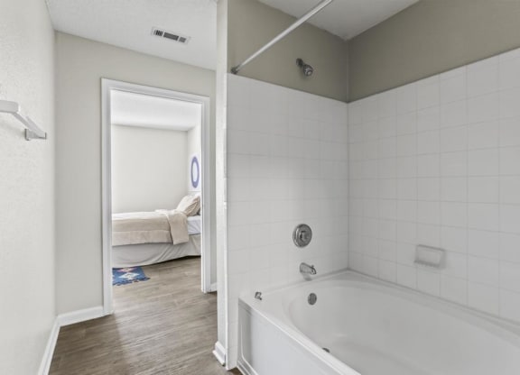 a white bathroom with a tub and a bedroom