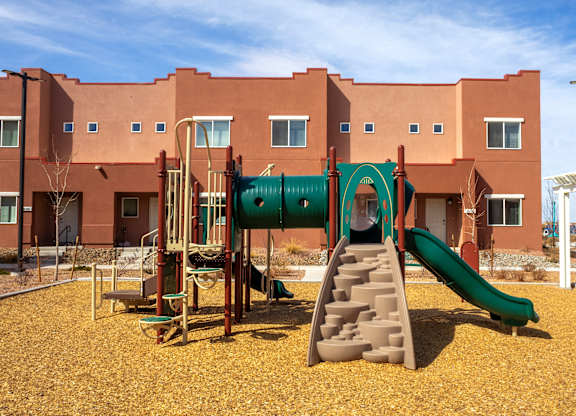 A playground with a green slide in front of a red building.