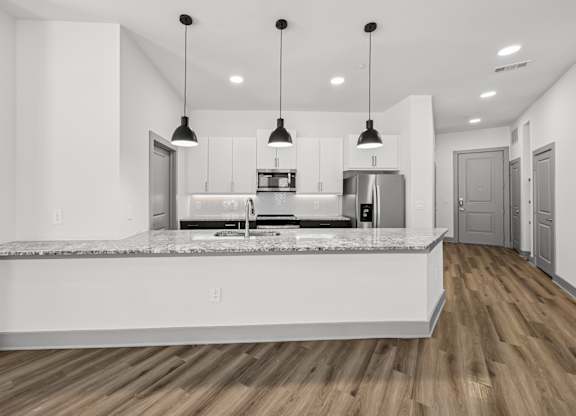 A modern kitchen with a marble countertop and pendant lights.