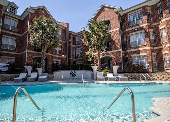 A swimming pool in front of a red brick building with palm trees.
