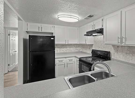 A black refrigerator is in a kitchen with white cabinets.