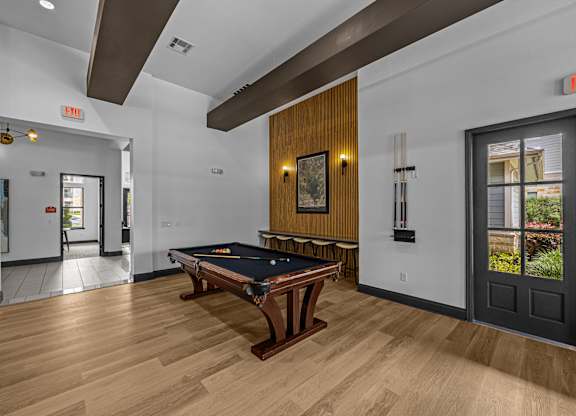 A pool table is in the middle of a room with a door to the left and a window to the right.