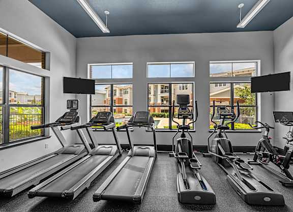 A gym with treadmills, exercise bikes, and a view of the outside.