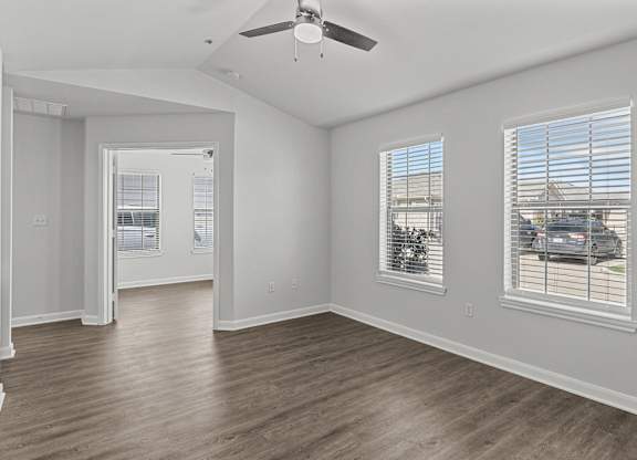 an empty living room with a ceiling fan and three windows