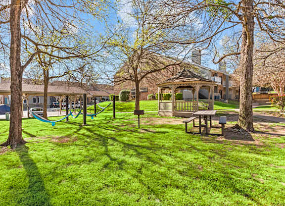 A playground with a swing set and a picnic table is surrounded by trees.