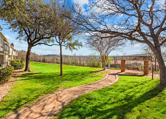 A pathway leads through a grassy area with trees and a bench.