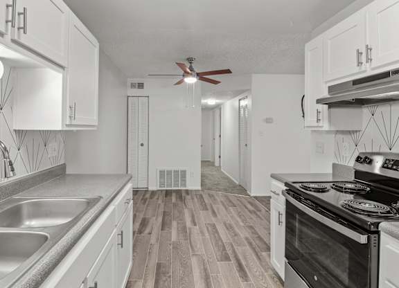 an empty kitchen with white cabinets and stainless steel appliances and a ceiling fan