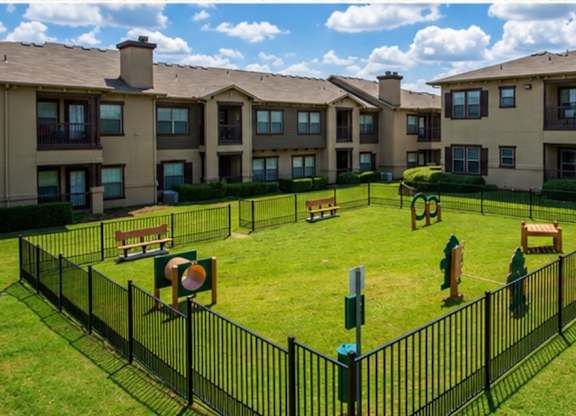 A black fence surrounds a green lawn in front of apartment buildings.