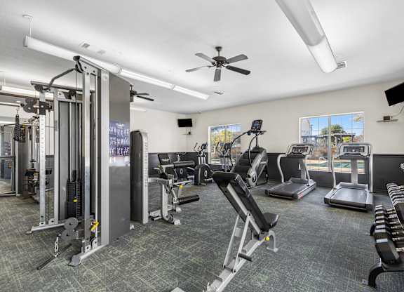 A well-equipped gym with various exercise machines and a ceiling fan.