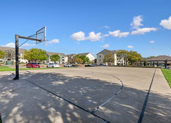 A basketball court with a hoop and a red car in the background.