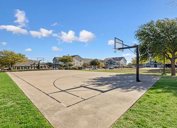 A basketball court is surrounded by grass and trees.