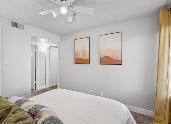 A bedroom with a bed, a ceiling fan, and two framed pictures on the wall.