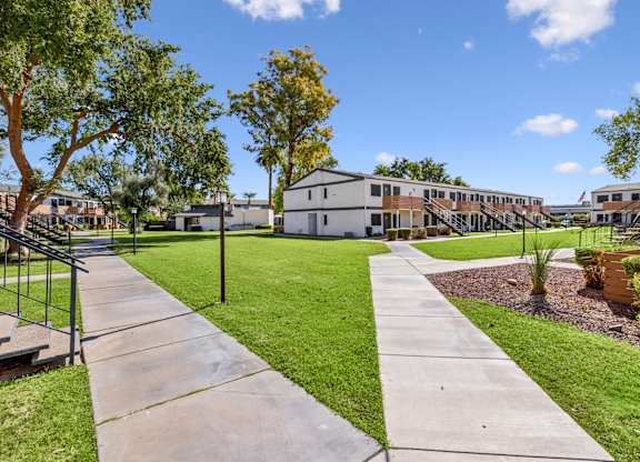A sunny day at a park with a walking path and green grass.
