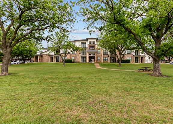 A grassy area with trees and a building in the background.