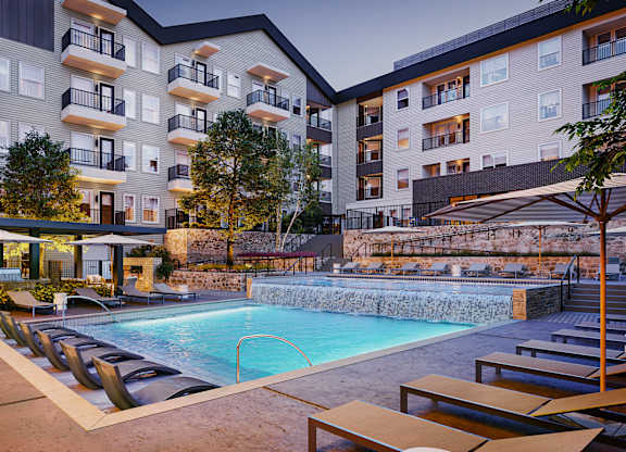 A swimming pool surrounded by lounge chairs and umbrellas in front of apartment buildings.