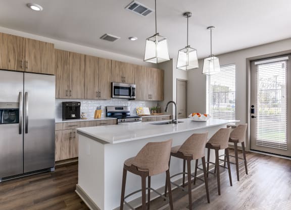 a kitchen with a large island with bar stools and a stainless steel refrigerator