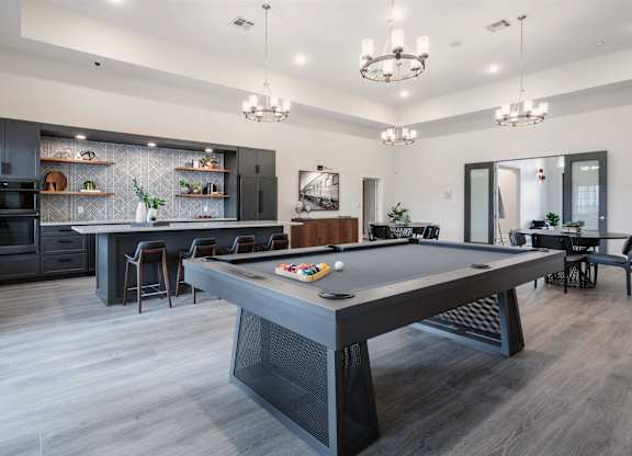 A pool table is in the middle of a room with a kitchen in the background.