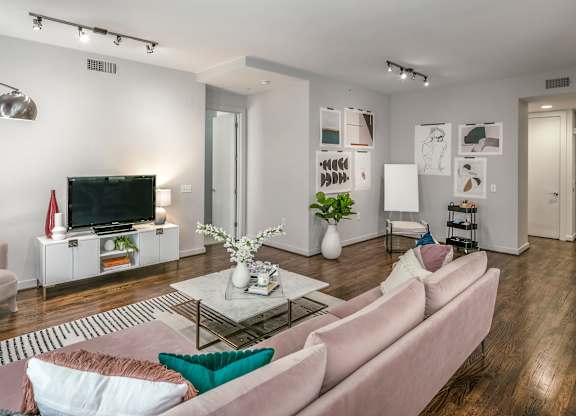 A living room with a pink couch and a television on a white cabinet.