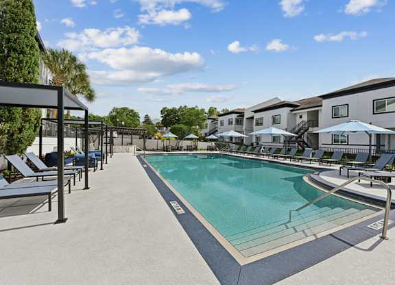 A swimming pool surrounded by sun loungers and umbrellas.