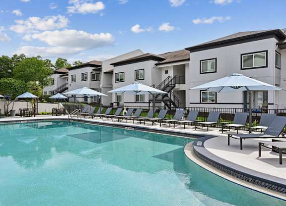 A swimming pool with sun loungers and umbrellas in front of apartment buildings.